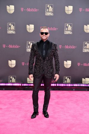 Attendee in black velvet blazer and sunglasses posing on pink carpet at entertainment event.