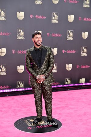 Guest in sparkly black tuxedo standing on personalized floor marker at red carpet event.
