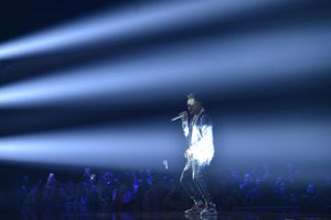Performer silhouetted against dramatic blue spotlights during concert performance.