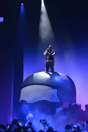 Performer standing atop curved platform with dramatic blue and white stage lighting.