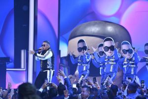 Stage performance with blue lighting and multiple digital screen displays showing performer images.