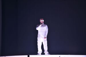 Performer in all white outfit standing on darkened stage during concert.