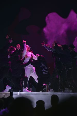 Dancers in white and black outfits performing under purple stage lights.