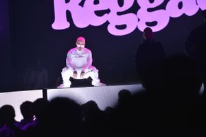 Performer in white outfit crouching on illuminated stage with purple text backdrop.