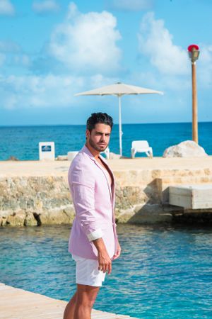 Stylish summer outfit with pink blazer and white shorts against coastal backdrop.
