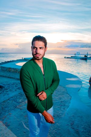 Person in green sweater and jeans standing on coastal walkway at sunset.