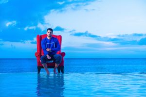 Red vintage chair with person sitting in it positioned at edge of infinity pool overlooking ocean.