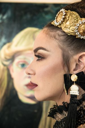 Ornate gold crown and tassel earring detail in dramatic profile portrait.