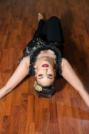 Artistic portrait of someone lying on wooden floor in black attire with vintage-inspired styling and red lipstick.