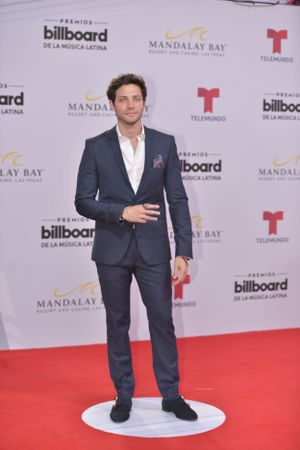 Well-dressed man in navy suit poses on red carpet at Billboard awards event.