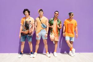 Group of men in colorful summer outfits pose against purple wall background.