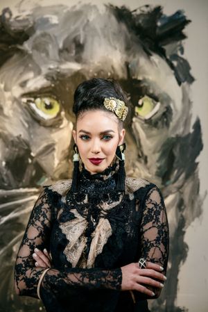 Dramatic portrait against large painted wolf artwork wearing black lace gothic-inspired outfit.