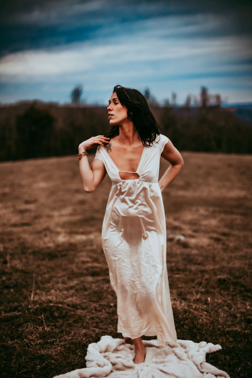 A dreamy portrait in a white dress standing on fabric against a mountainous backdrop.
