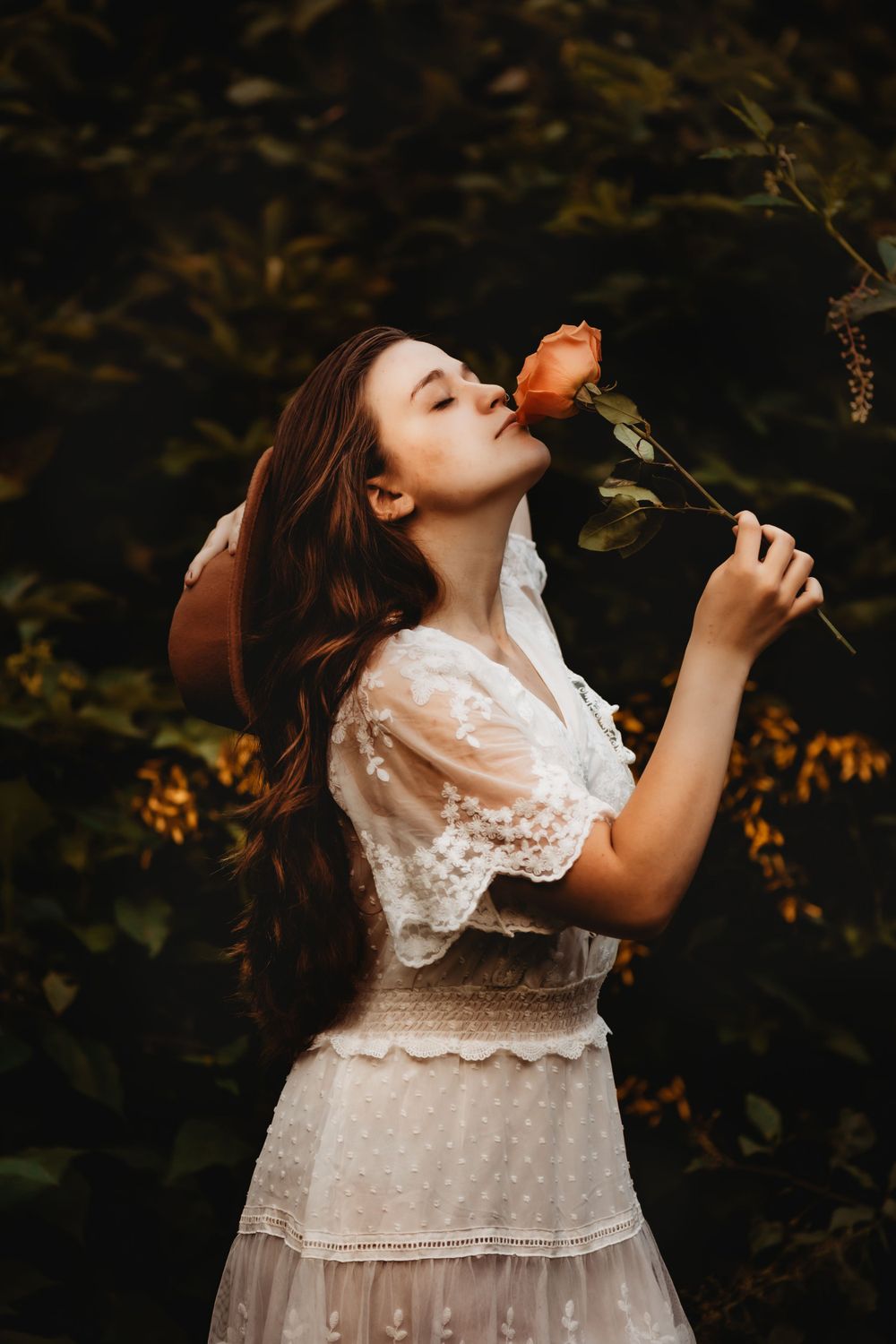 A vintage-styled portrait of someone smelling a red rose against a dark nature backdrop.
