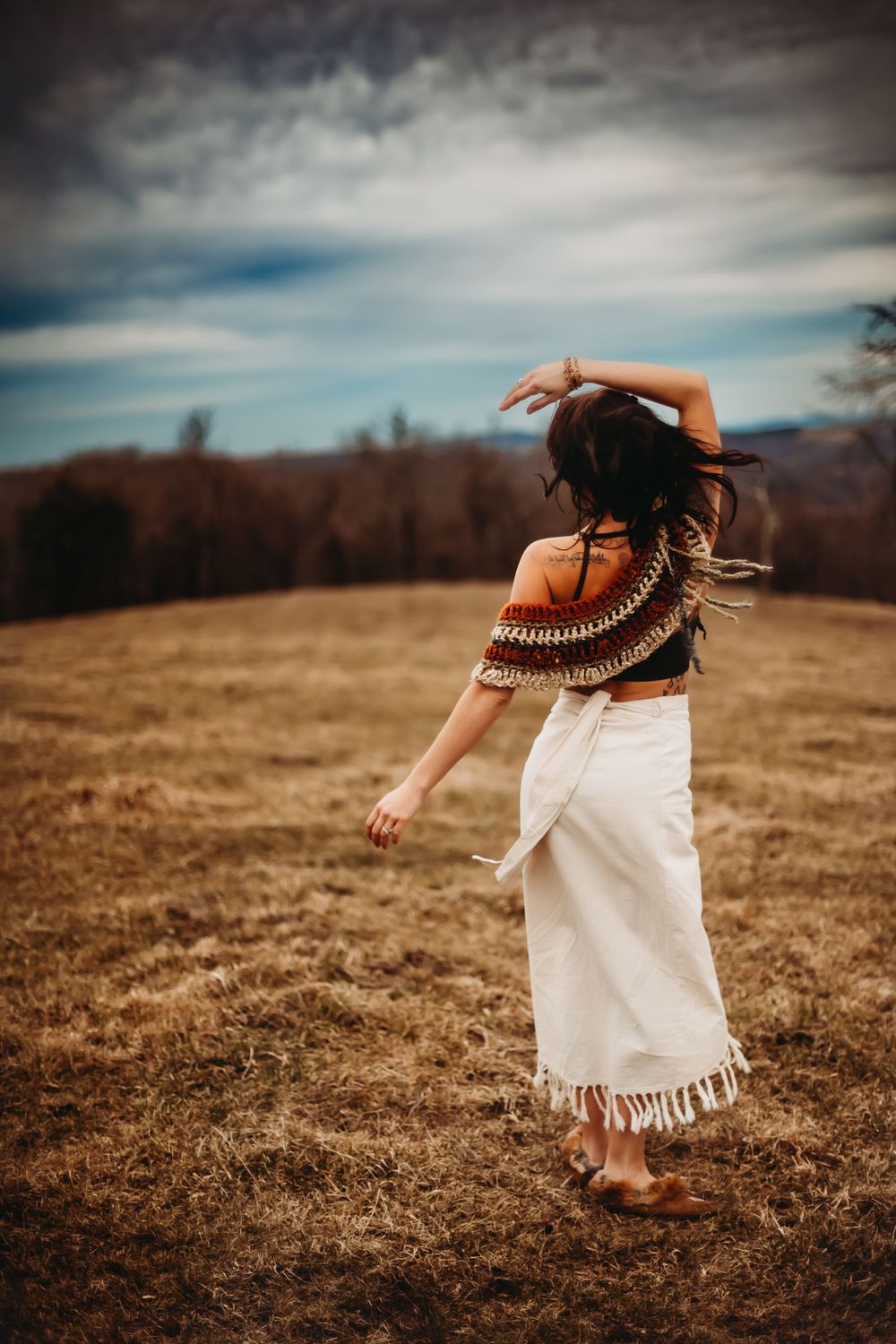A free-spirited dance movement captured in a rustic field under cloudy skies.