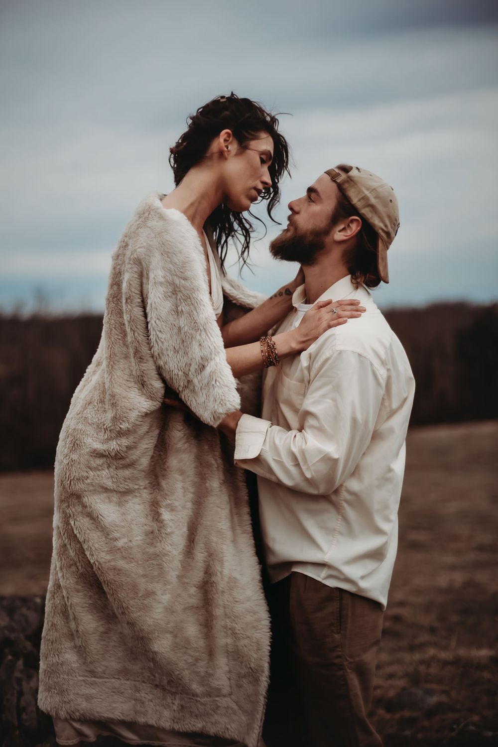 A tender moment between two people sharing laughter in casual attire on a hilltop.