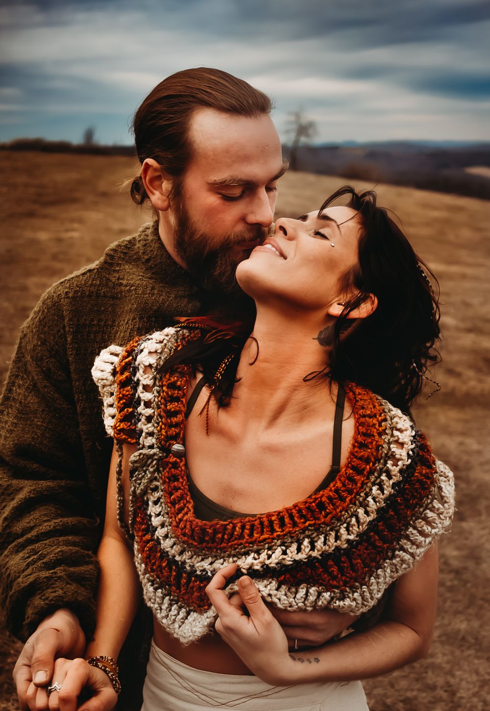 An intimate portrait of a couple embracing against a moody sky in warm autumn tones.