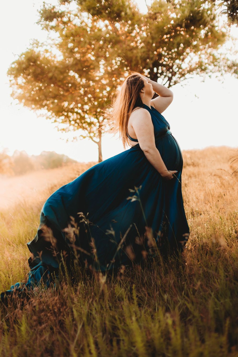 A blue gown flows gracefully in a golden field during sunset.