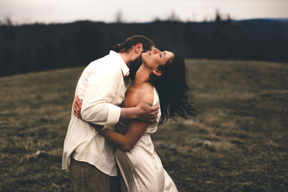 Couple embracing romantically in a field at sunset with dramatic lighting.
