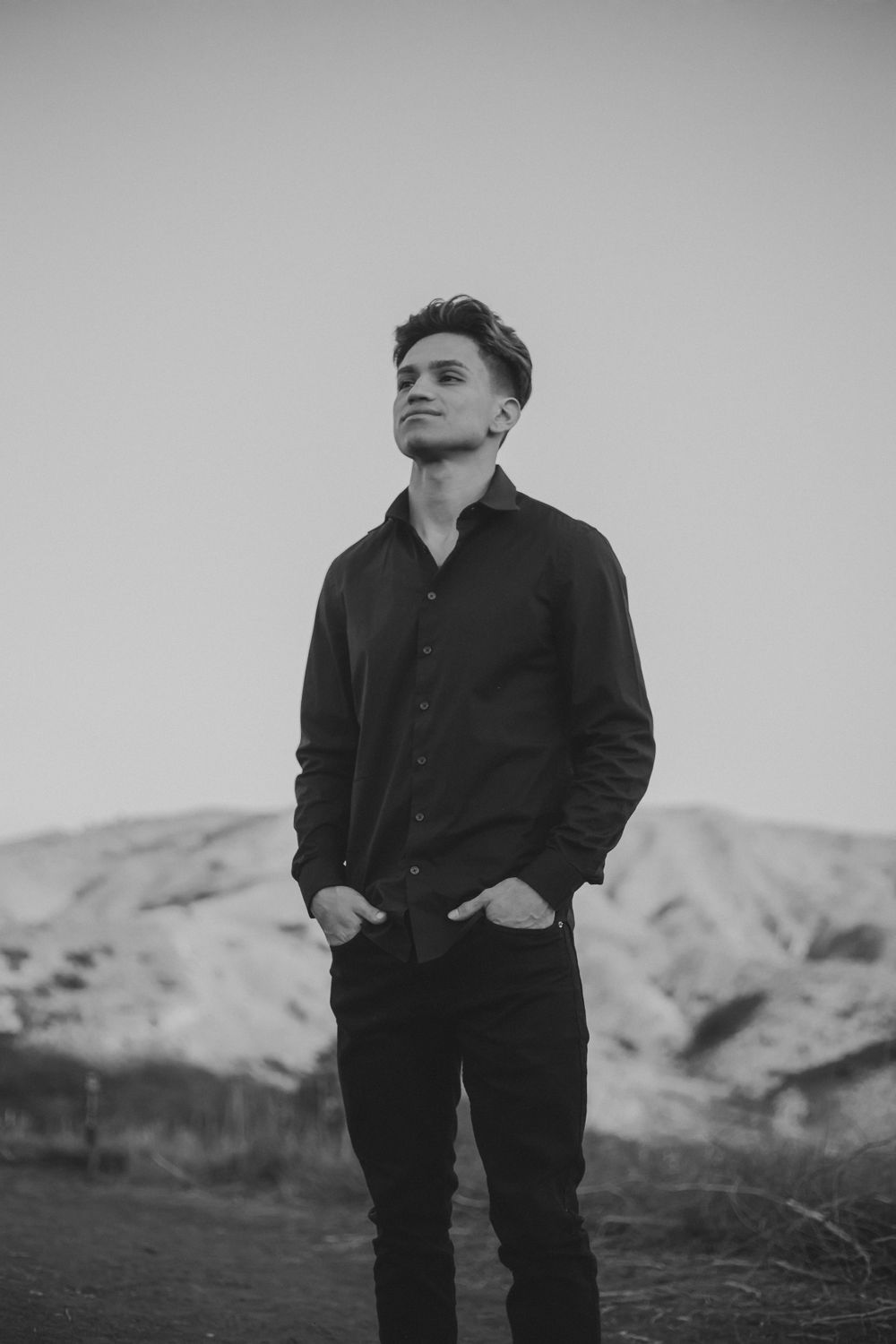 A black and white portrait photo showing man wearing dark clothing against a mountainous landscape in Anaheim California