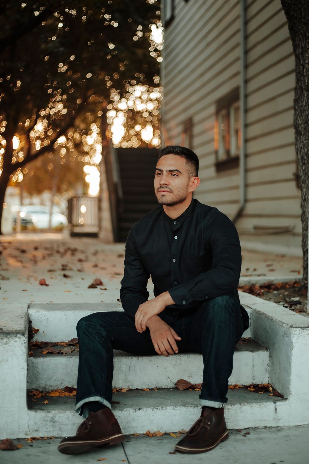 Man sits on white concrete steps at sunset wearing dark clothing and brown shoes as autumn leaves scatter around
