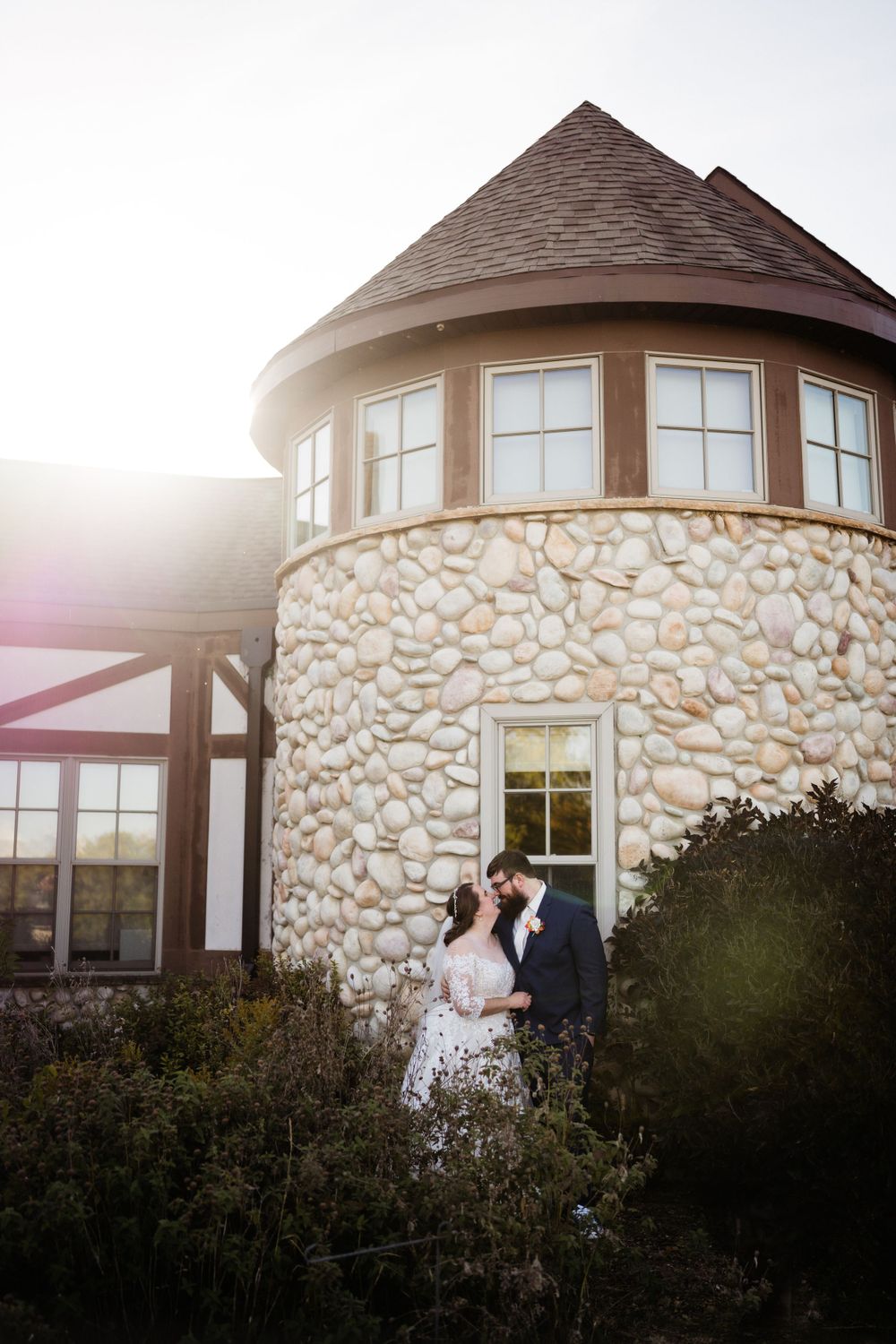 Couple posing outside a stone turret building at sunset with sunflare.