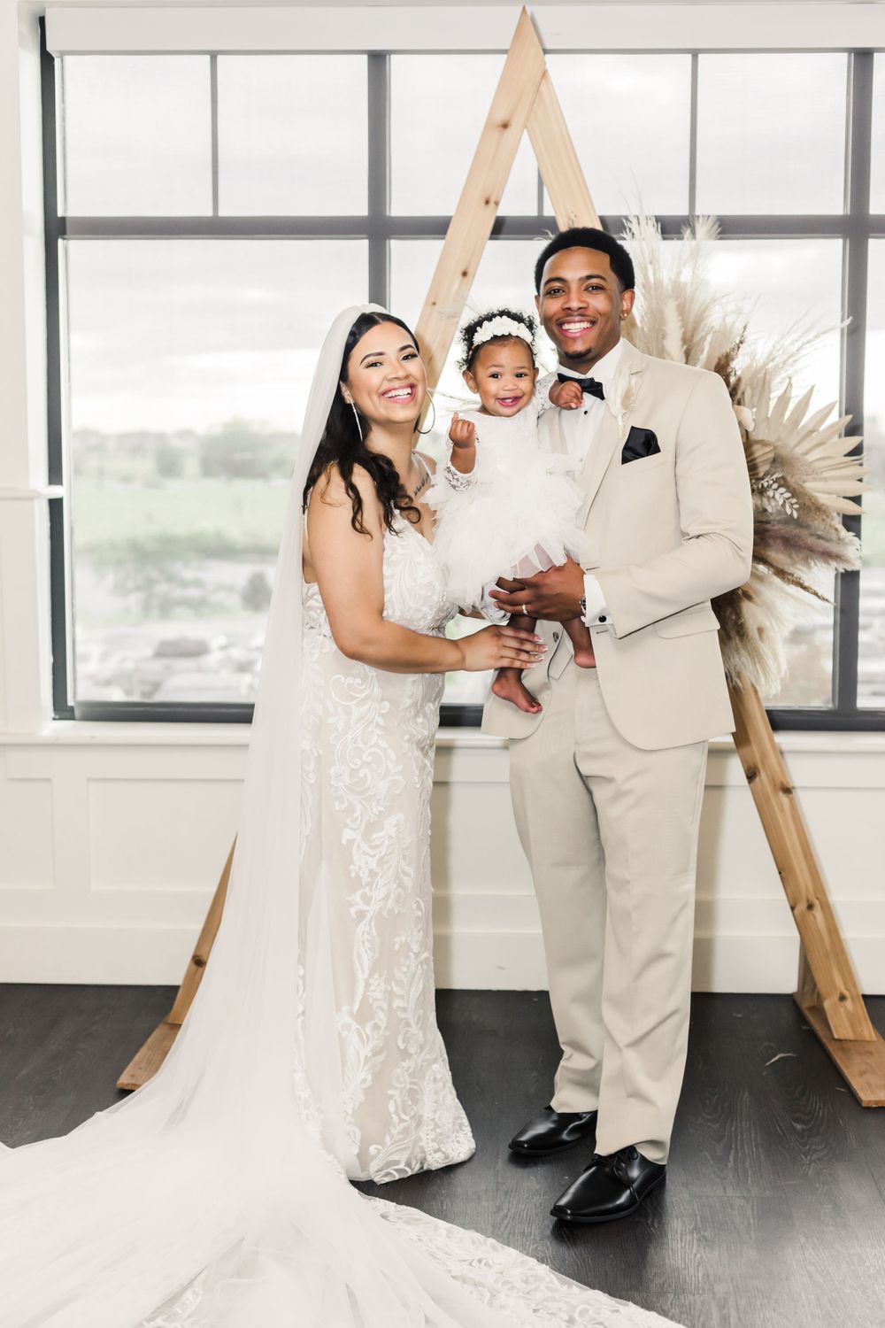 Wedding scene with wooden triangle arch backdrop and pampas grass decor.