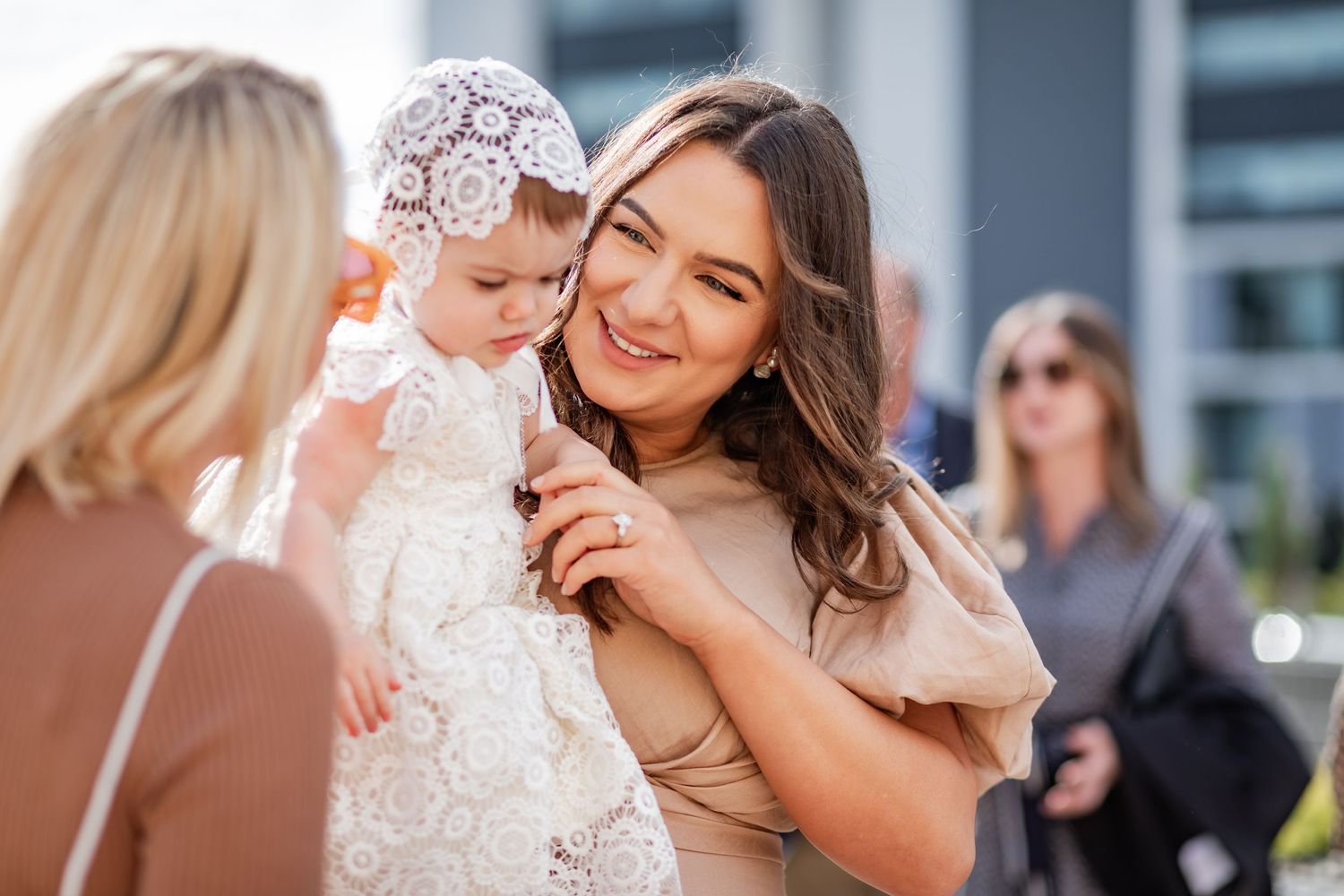 Outdoor gathering with baby in white lace christening gown.