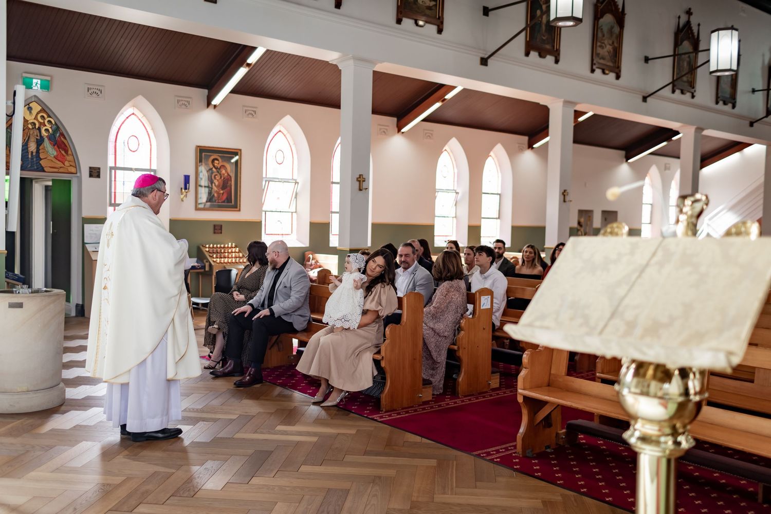 A religious service in progress inside a church with arched windows and wooden beams.