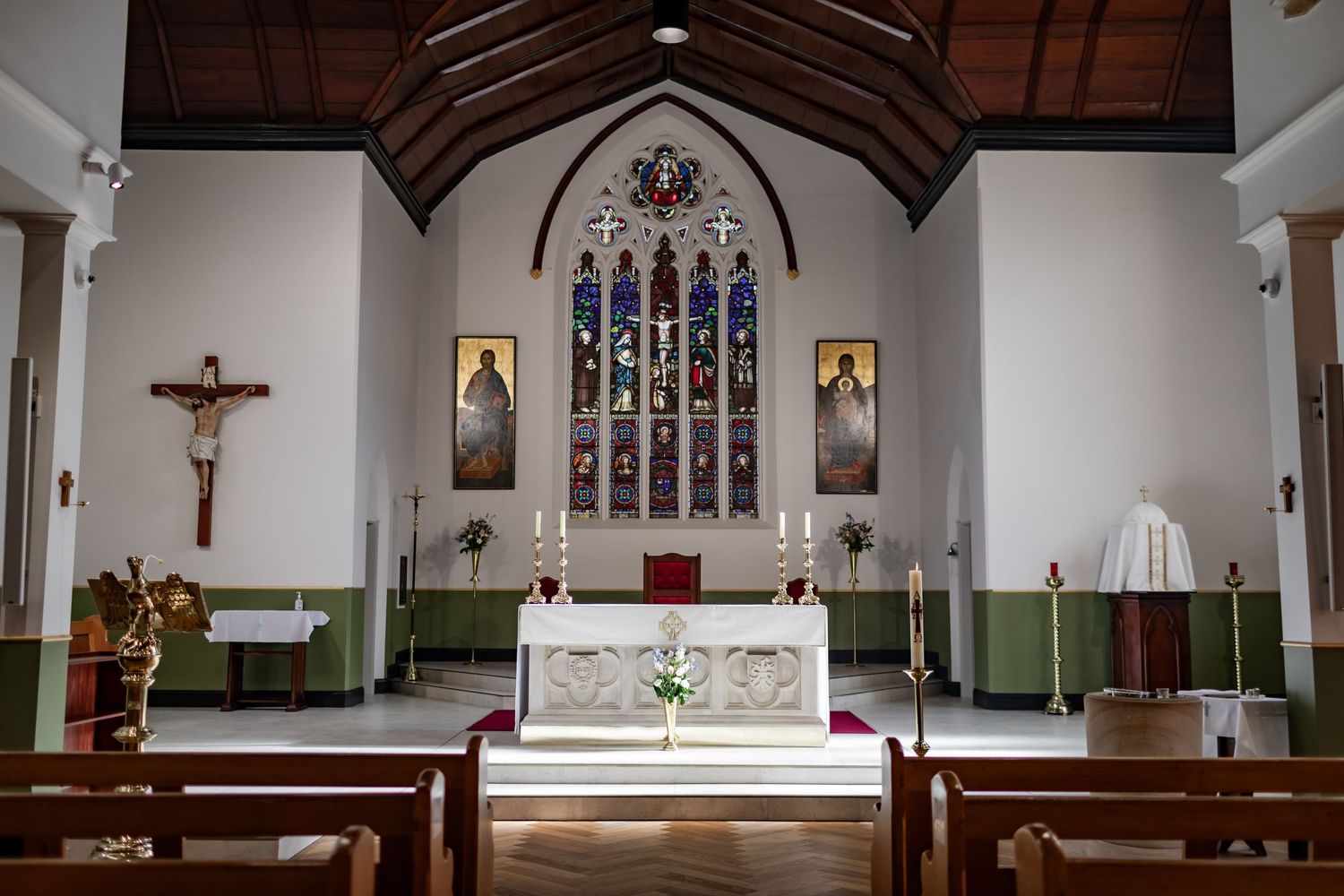 Interior of traditional church with stained glass window and wooden pews facing white altar.