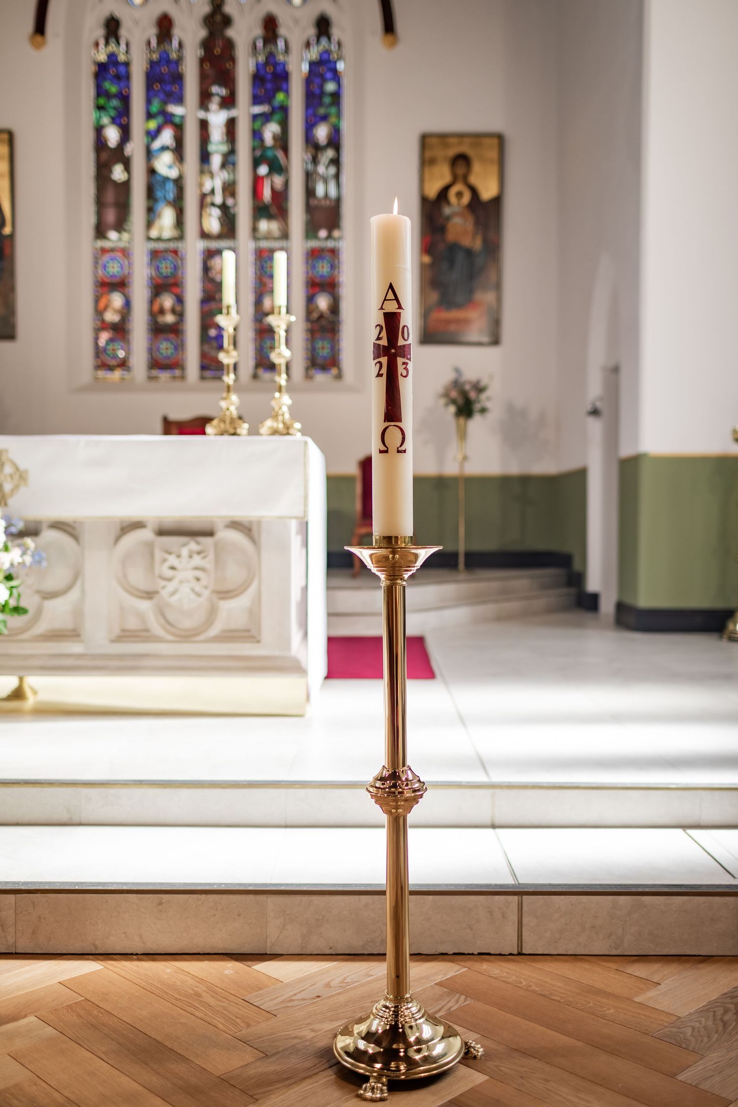 Ornate brass candlestick holder in church sanctuary with stained glass windows in background.