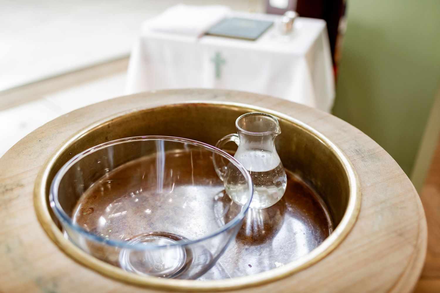 Close up of baptismal bowl filled with water on wooden surface in church setting.