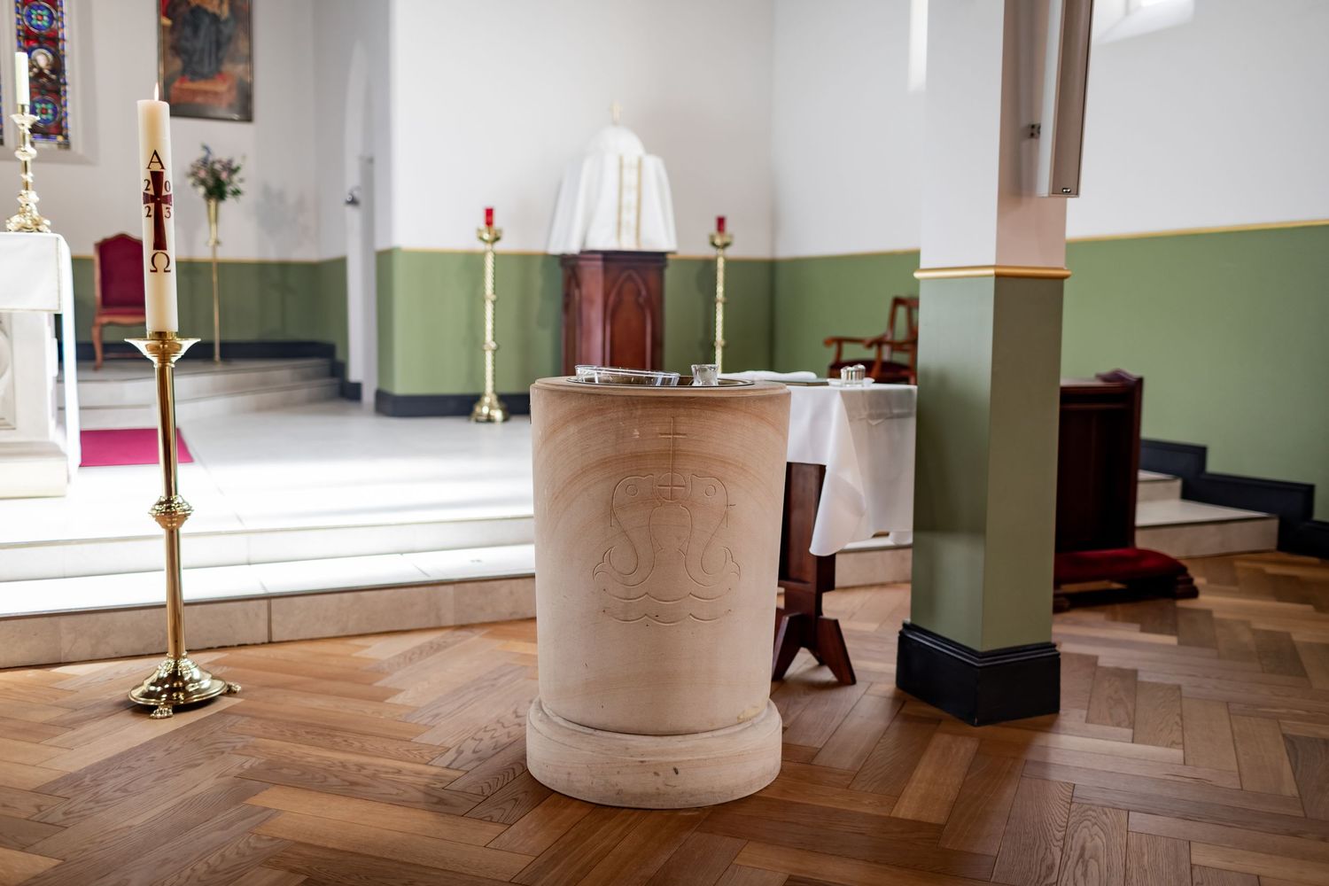Baptismal font in church interior with hardwood floors and green walls.