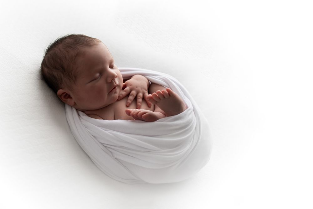 Newborn baby girl on white blanket backlit showing off her facial features.