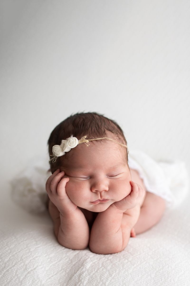 Newborn baby girl on a white blanket in the froggy position with a floral headband.