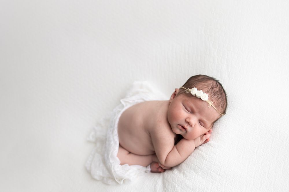 Newborn baby girl cuddled on a white blanket and white wrap across her bottom.