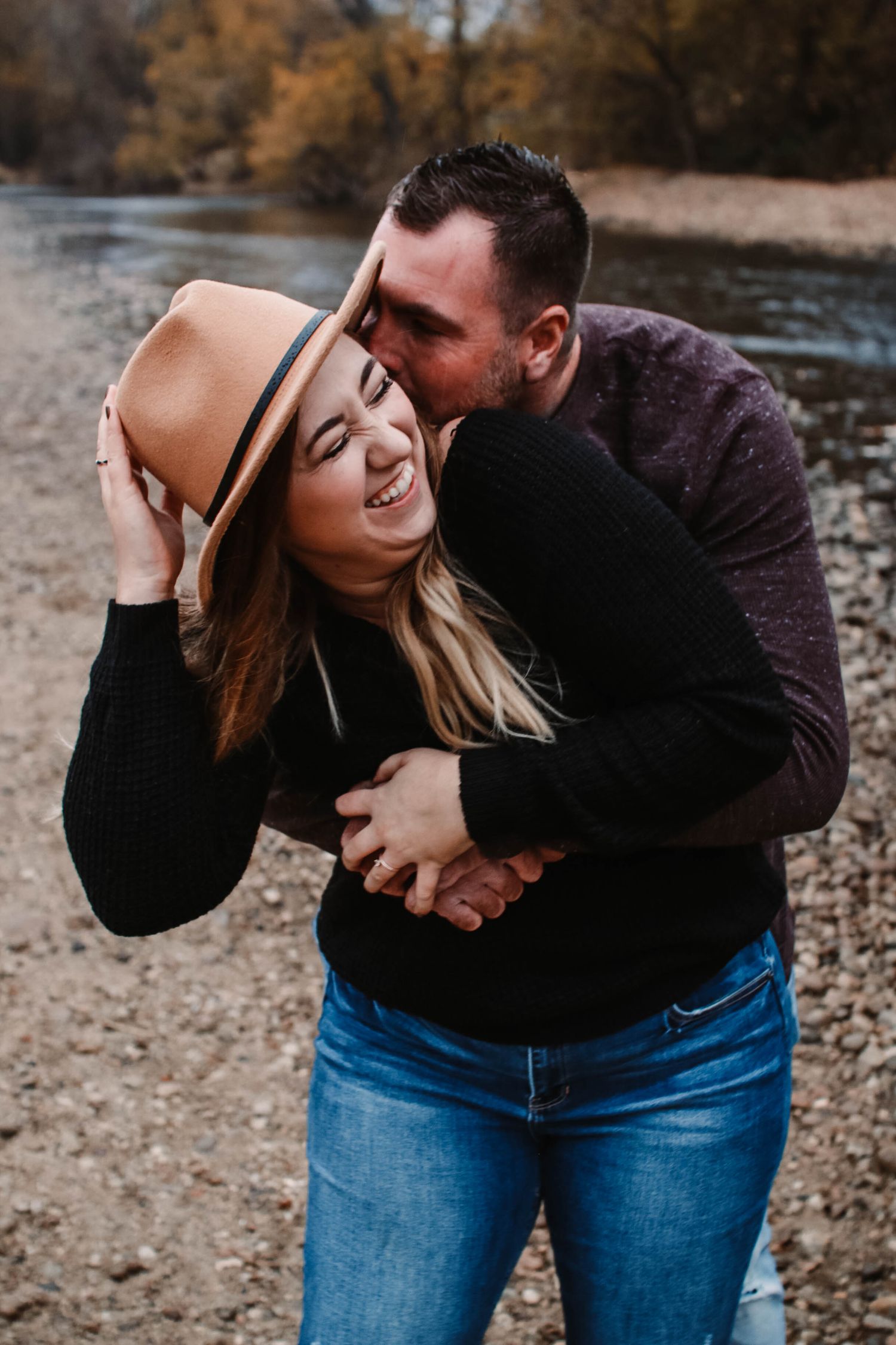 Playful couple sharing romantic moments outdoors by a river.
