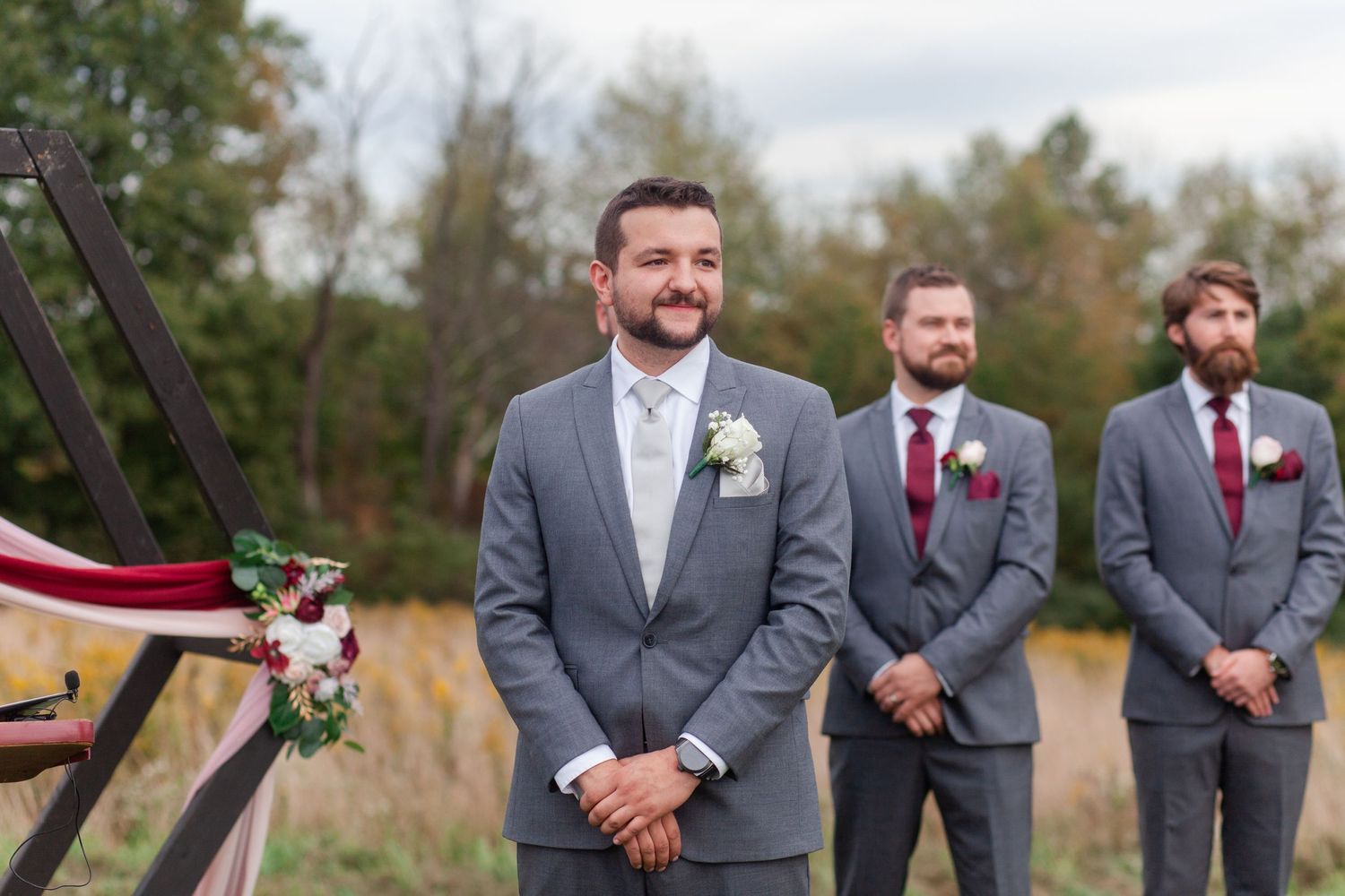 Wedding party members in grey suits stand at attention during outdoor ceremony.