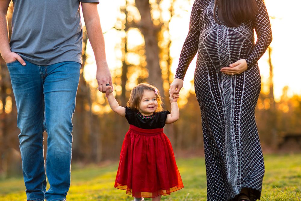 Family walking together outdoors with child in red dress between them.