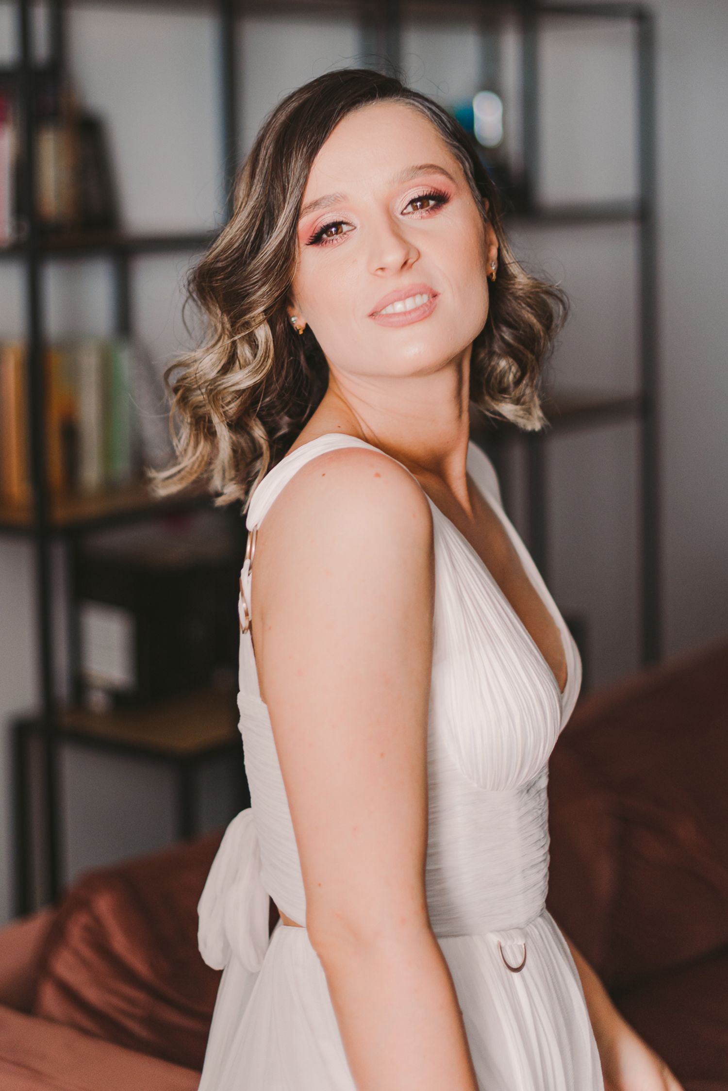 Woman in white dress posing gracefully against interior backdrop.