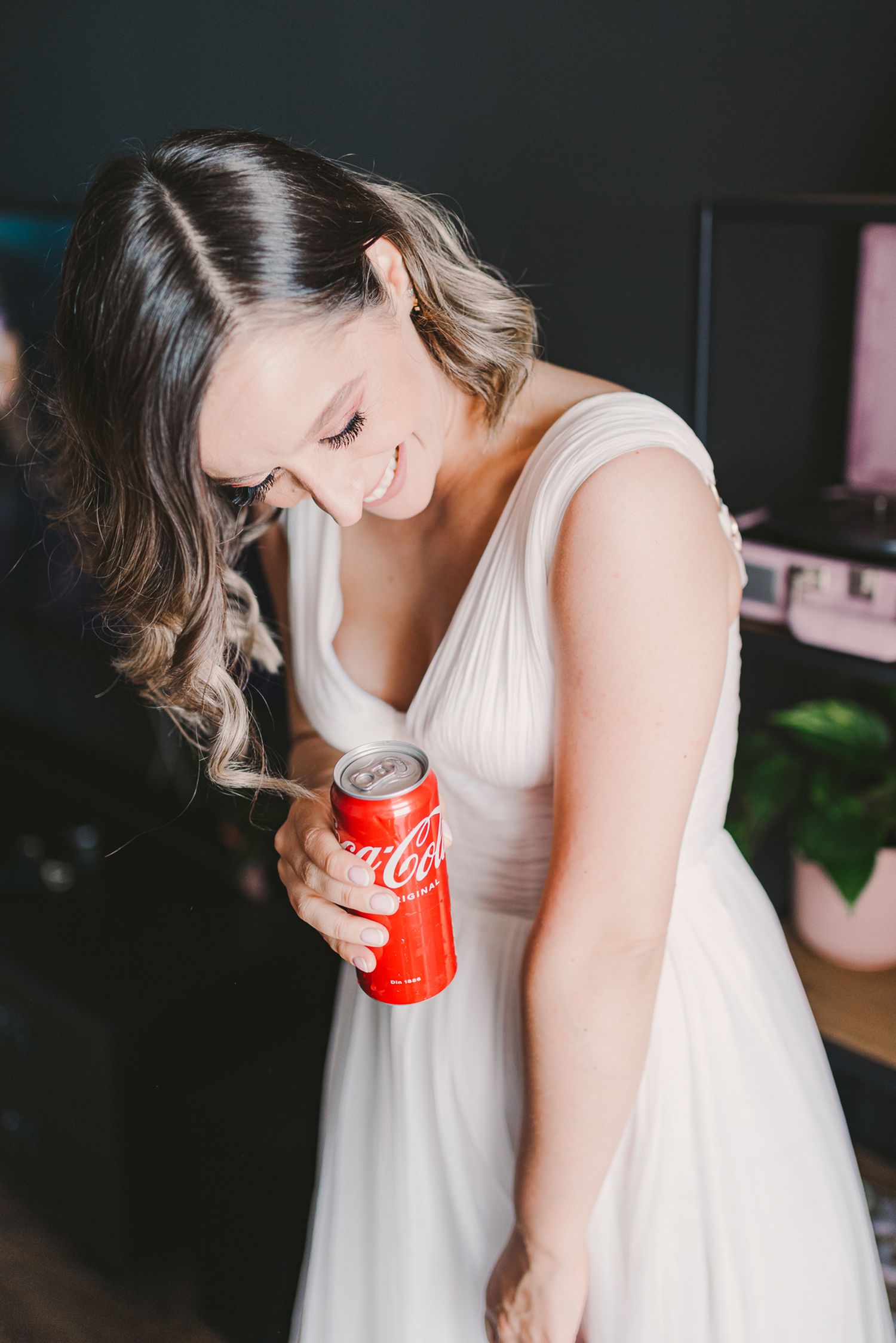 Woman in white dress drinking from Coca-Cola can in dimly lit room.