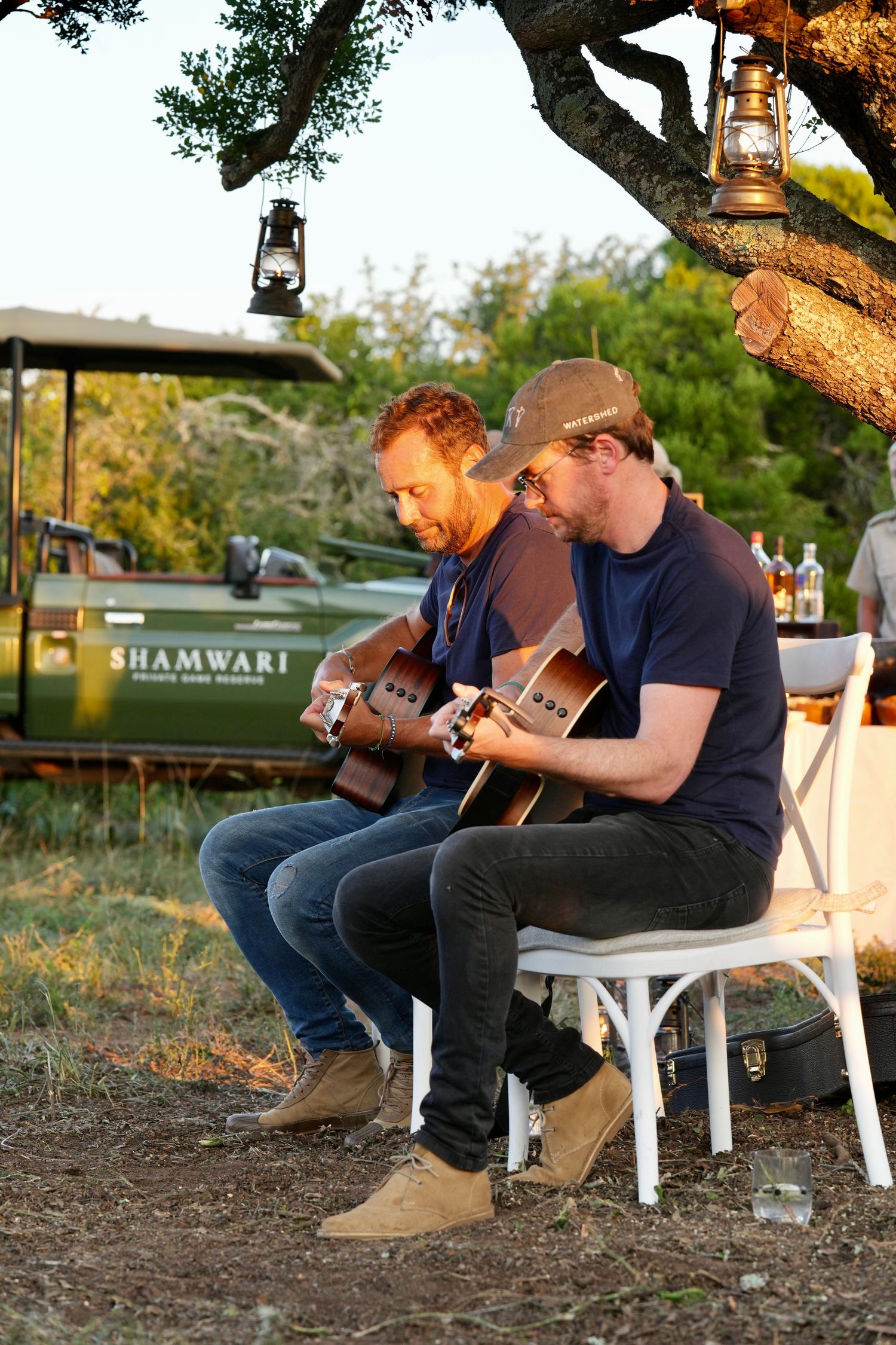 Musicians playing acoustic guitars while seated outdoors at sunset.
