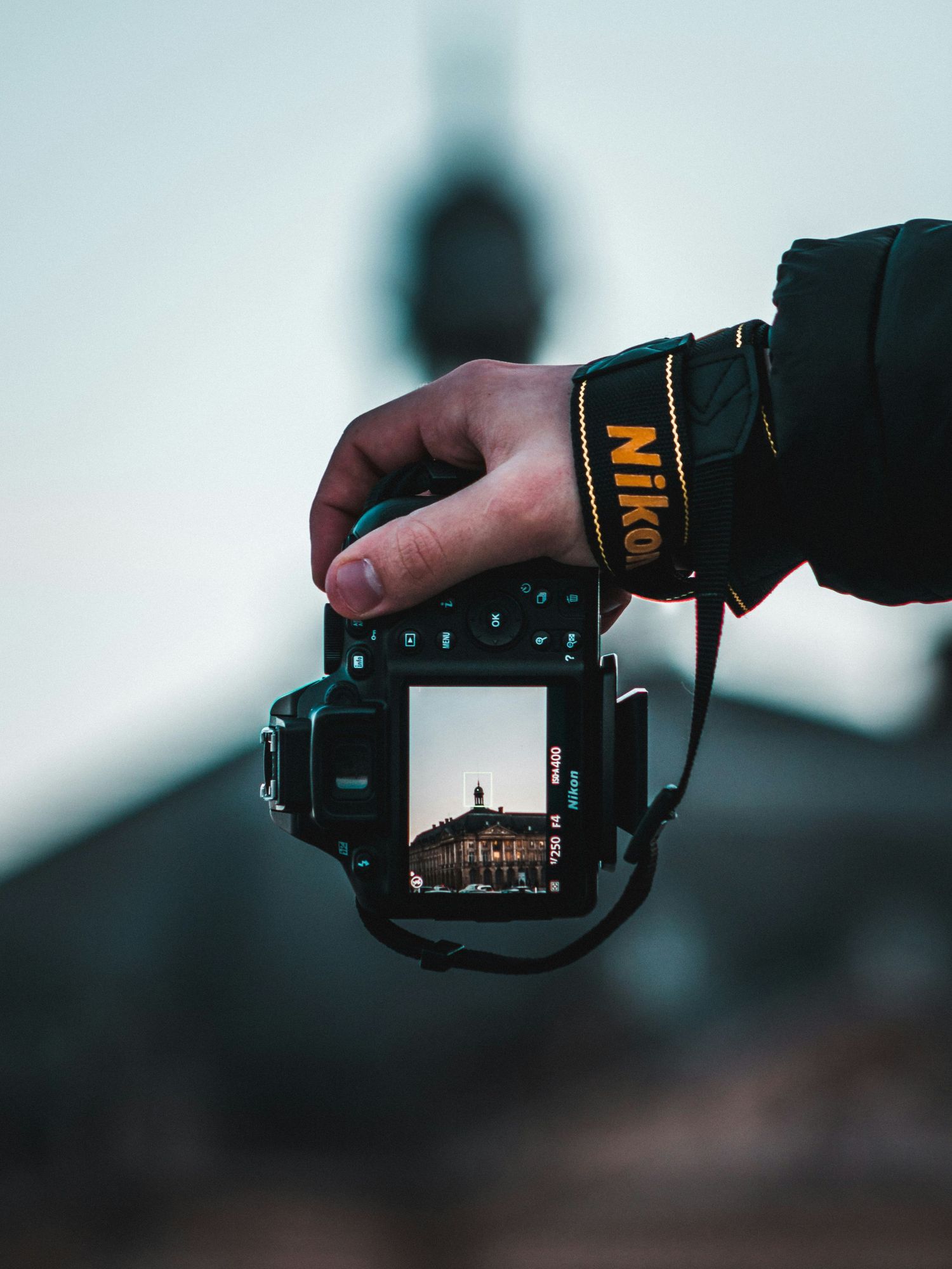 a hand holds a Nikon camera and the display reveals an old European building