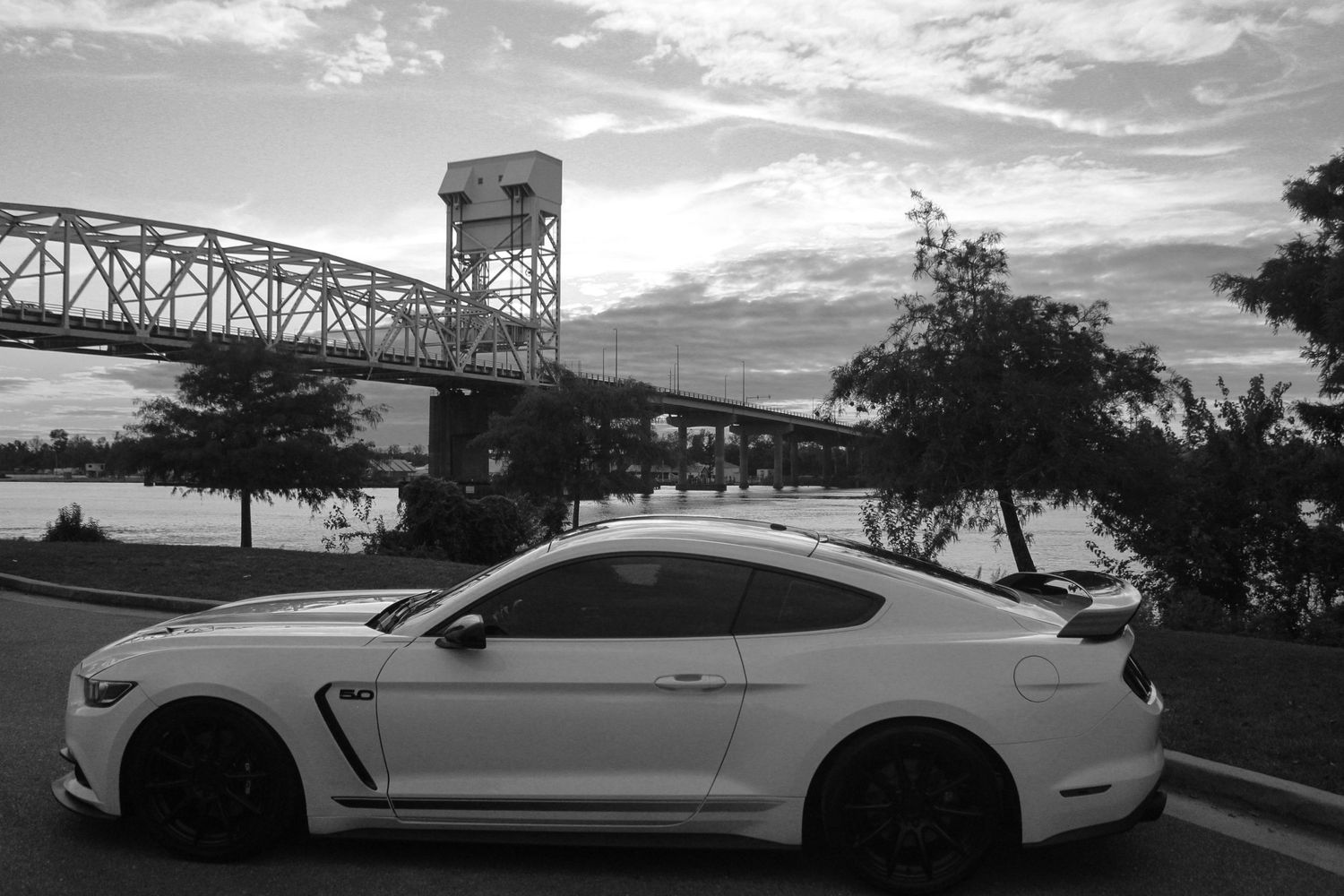 A white sports car parked near a bridge during sunset in black and white.