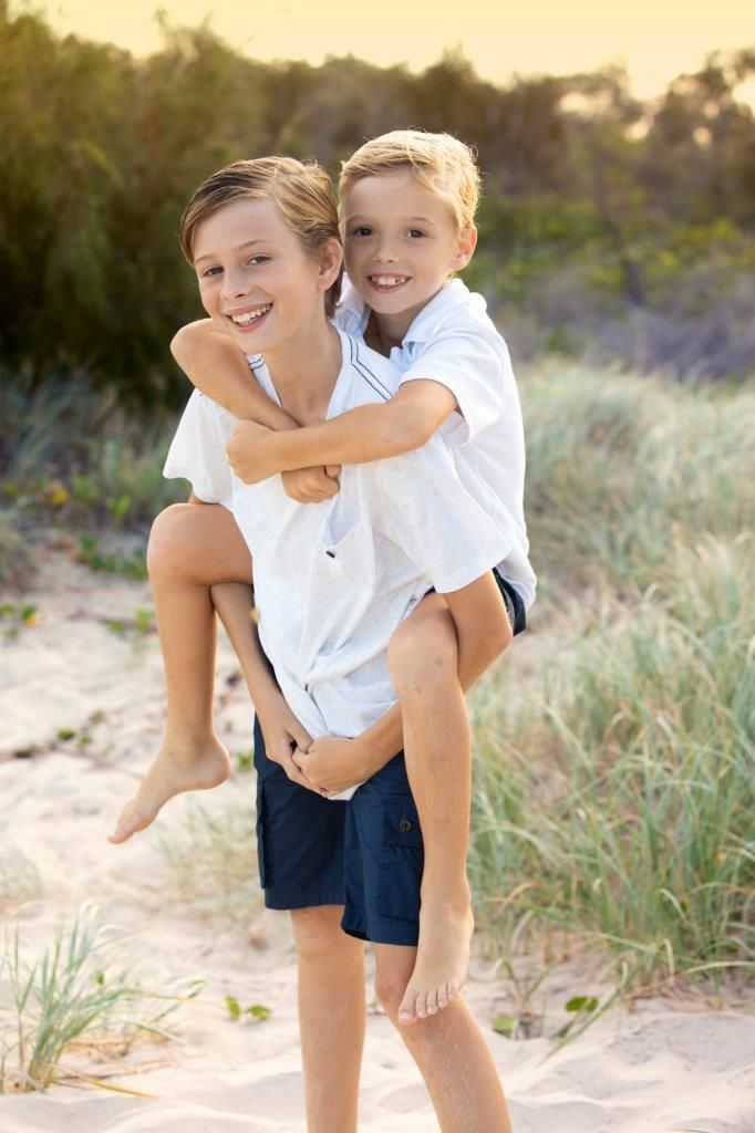 Playful beach portraits in white and navy outfits against coastal vegetation.