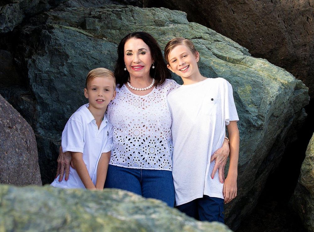 Family group poses together against rocky coastal backdrop at sunset.