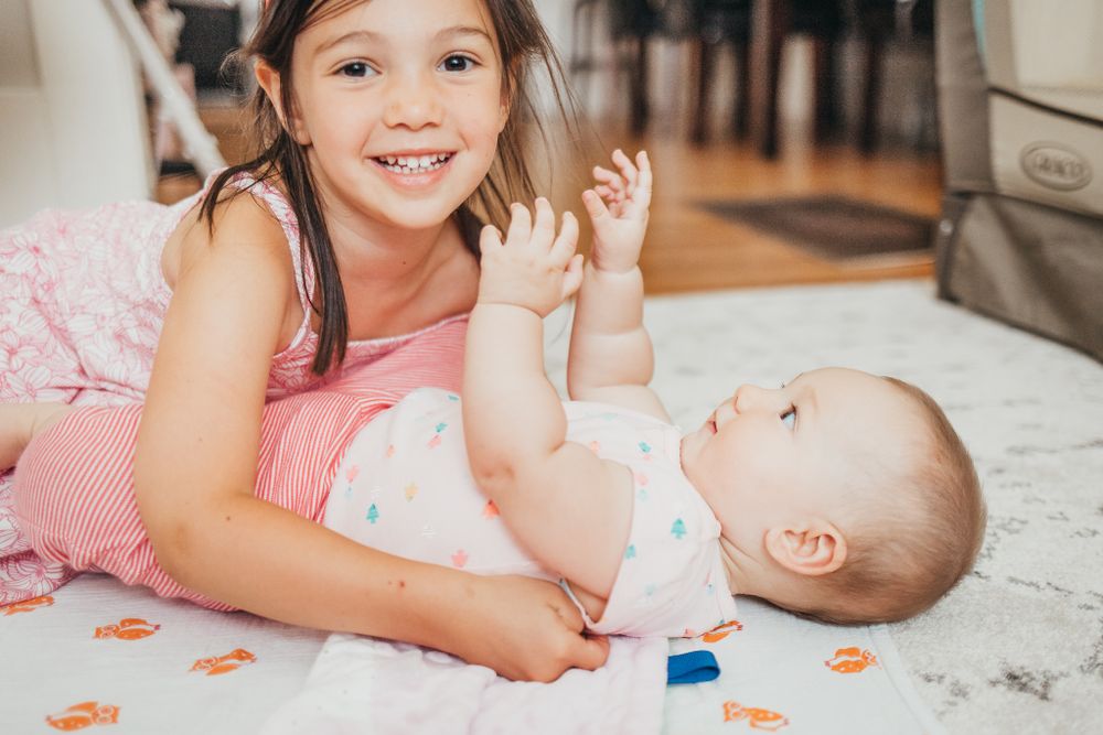 Two siblings sharing a sweet moment while playing on a white carpet with orange decorations.