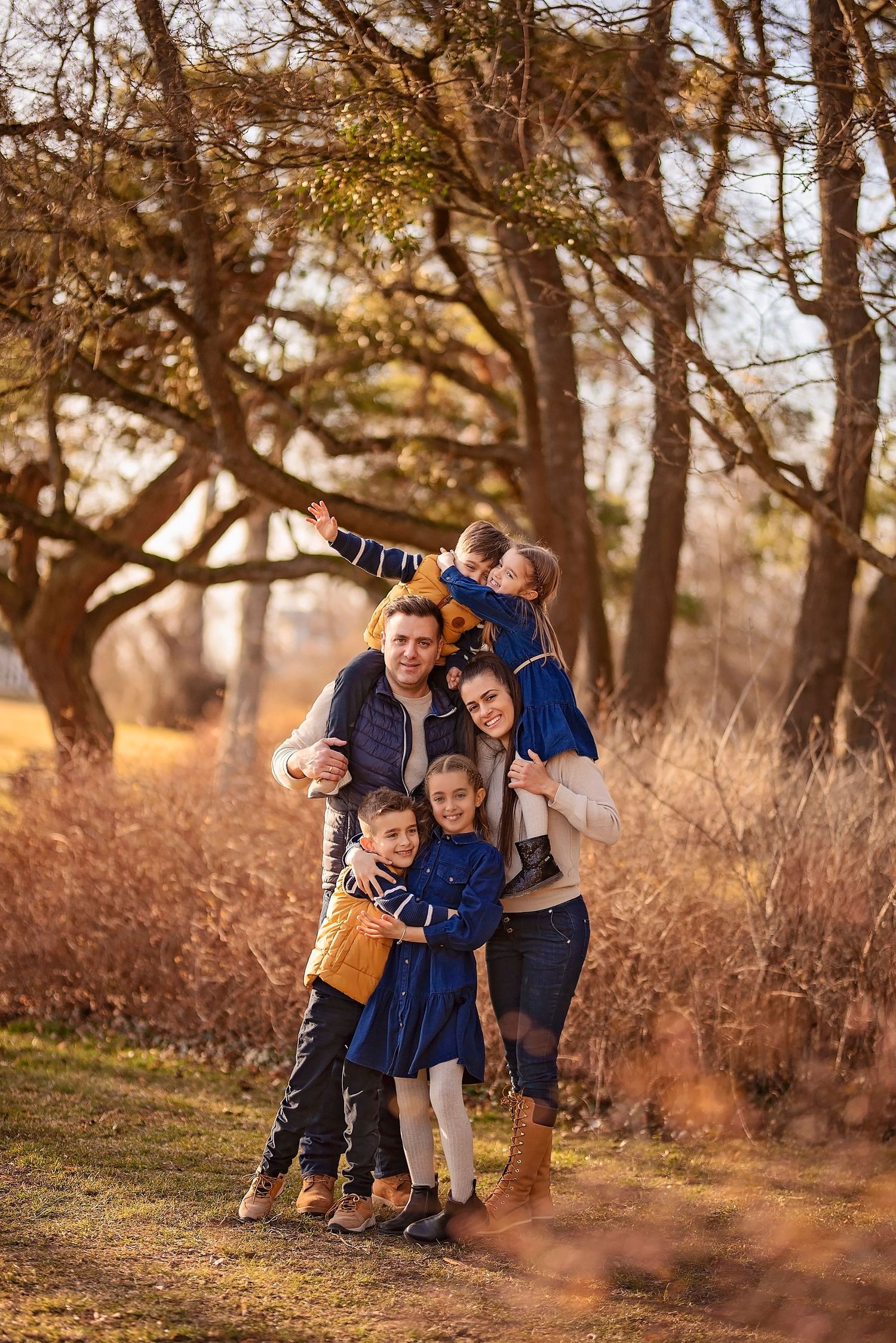 Family in blue outfits hugging and laughing together in a fall outdoor setting with trees in the background.