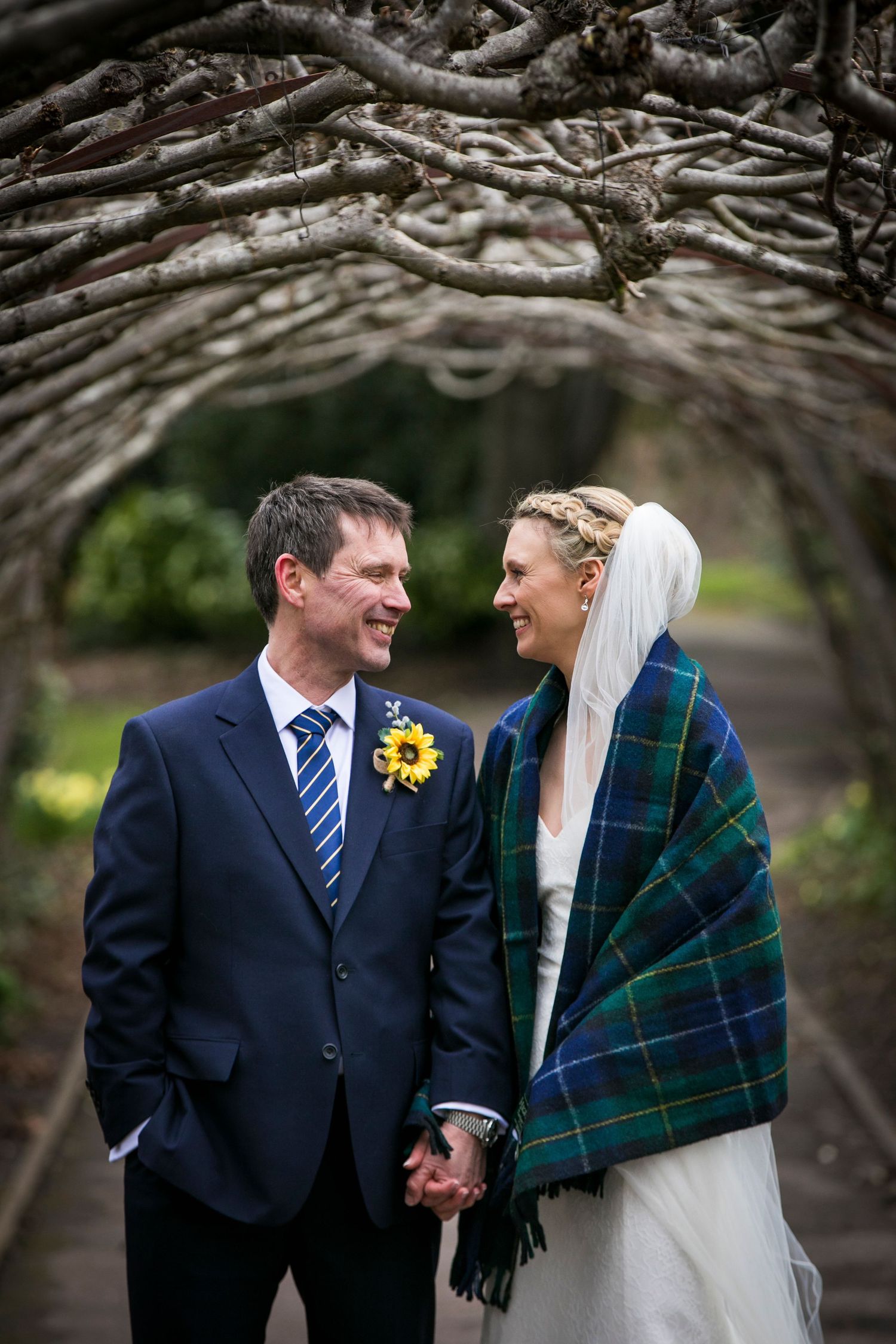 Couple shares an intimate moment under a natural branch archway in a garden setting.
