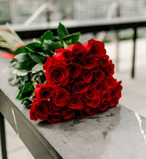 Fresh bouquet of vibrant red roses with green leaves resting on concrete ledge.